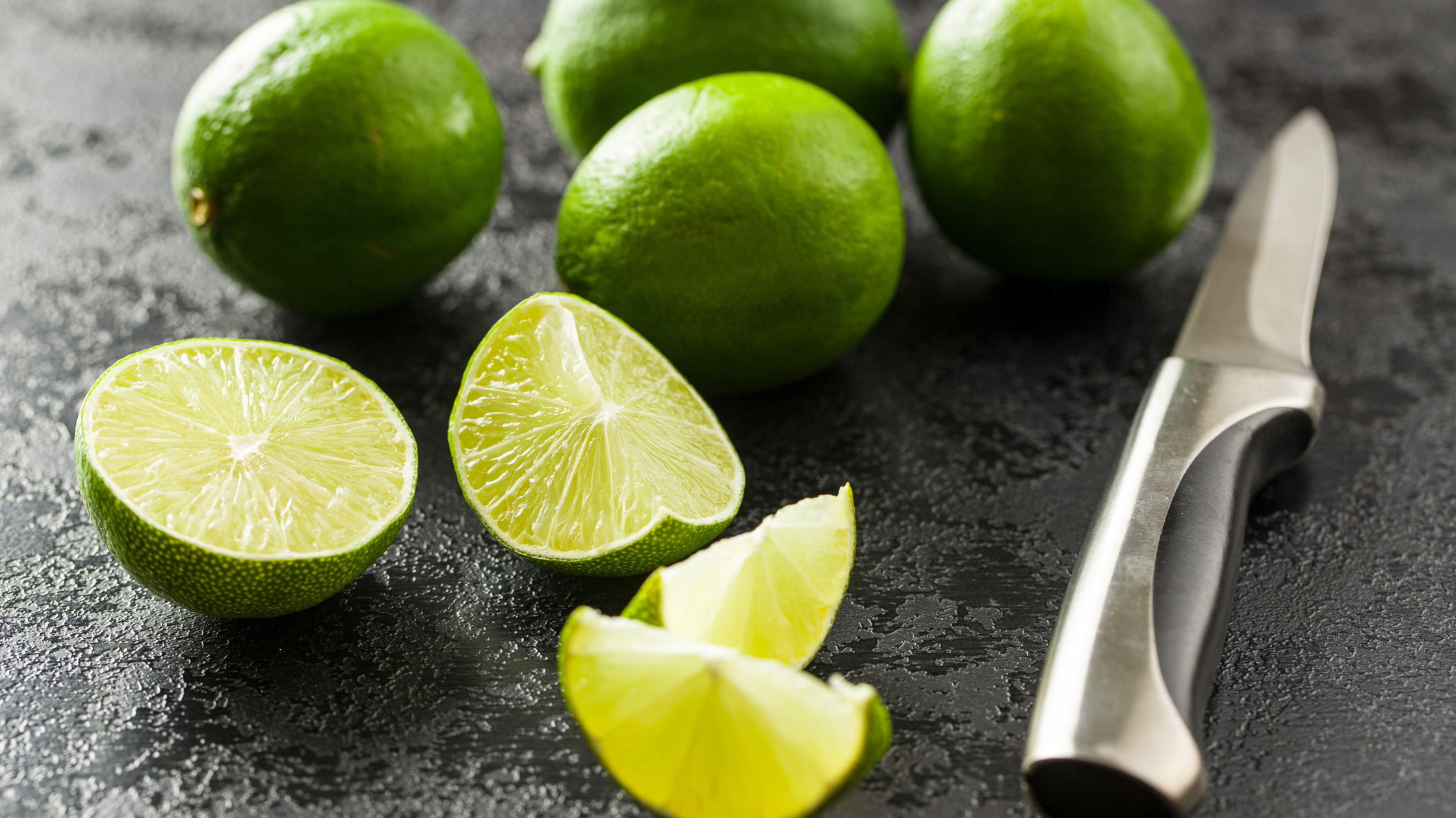 limões verdes sobre uma bancada com uma faca ao lado, para ilustrar os benefícios do limão