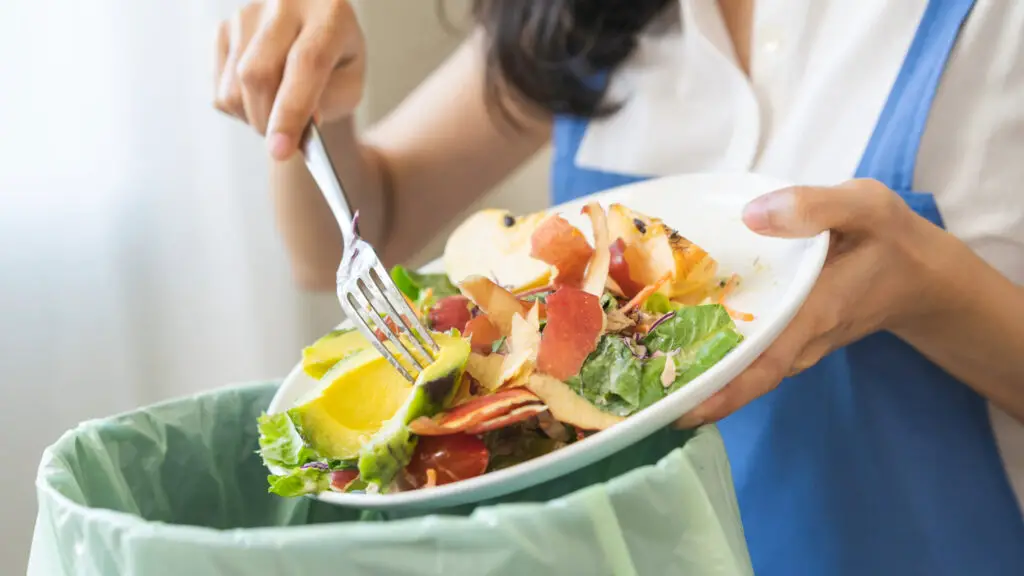 uma mulher jogando comida boa no lixo por não saber como evitar o desperdício de alimentos em casa